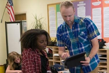 一个学生和老师在教室里拿着平板电脑交谈